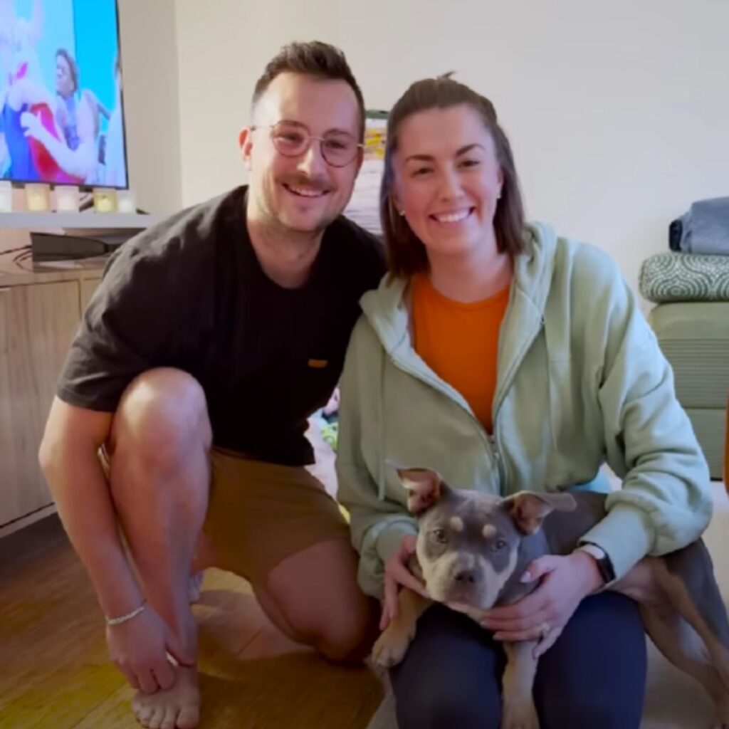 a man and a woman with a dog in the house take a picture