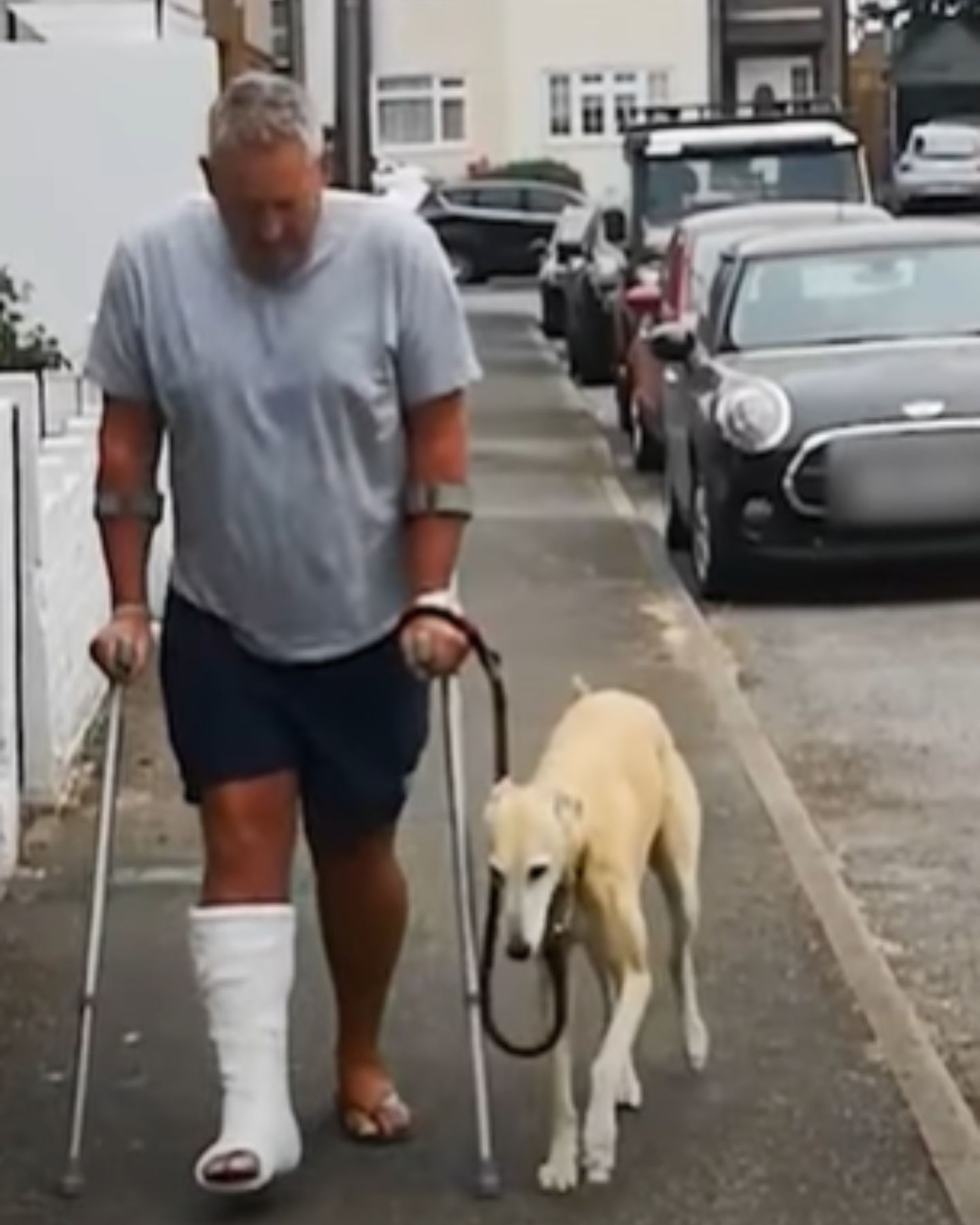 a man with cash on leg walking with his dog