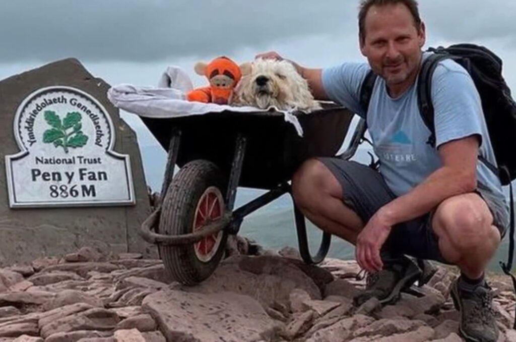 a man takes a picture with his dog in a cart on the mountain