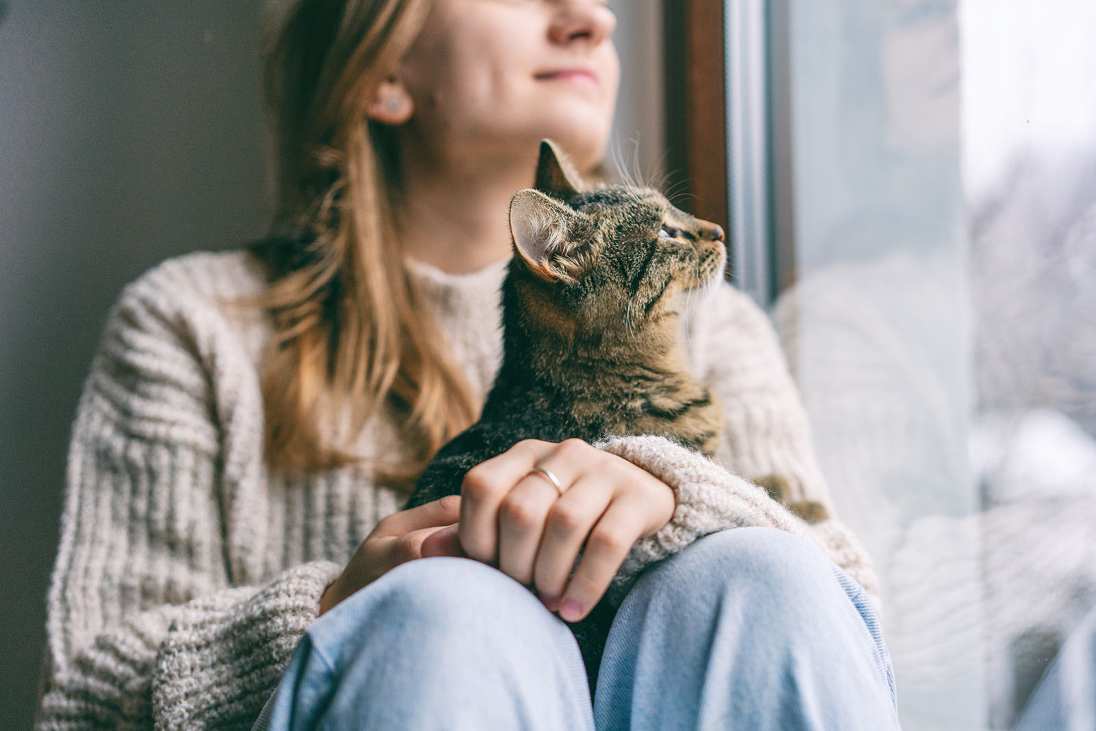 young woman with cat in lap looking through the window